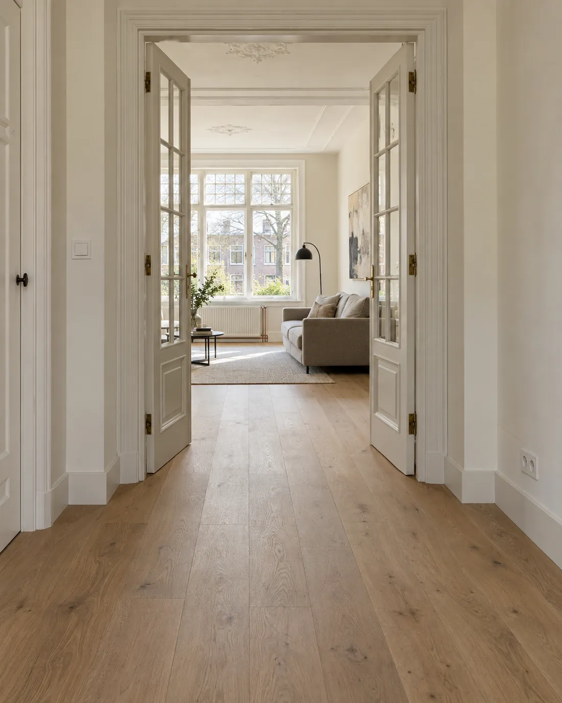 Hal met nieuwe eiken vloer en doorkijk door gerestaureerde en-suite deuren naar de woonkamer