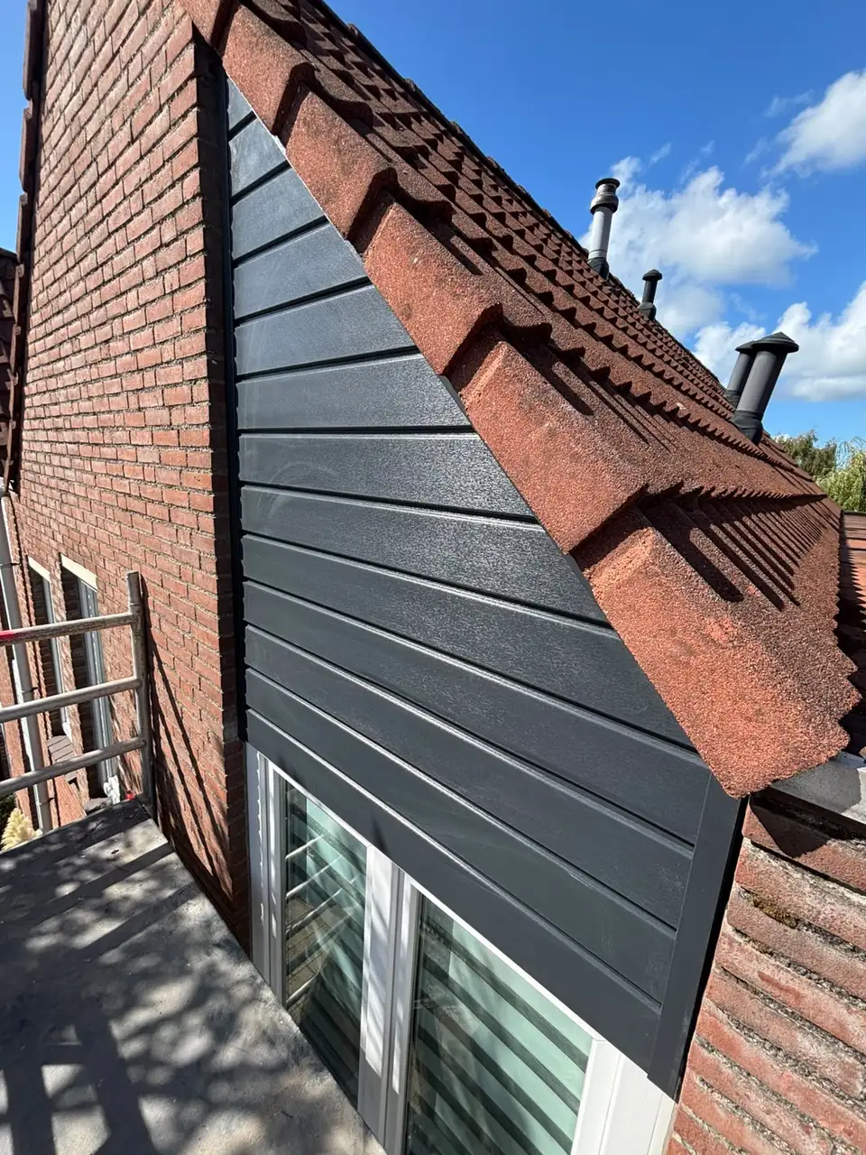 Topgevel met antracietkleurige horizontale gevelpanelen onder de dakpannen, gezien vanaf de steiger