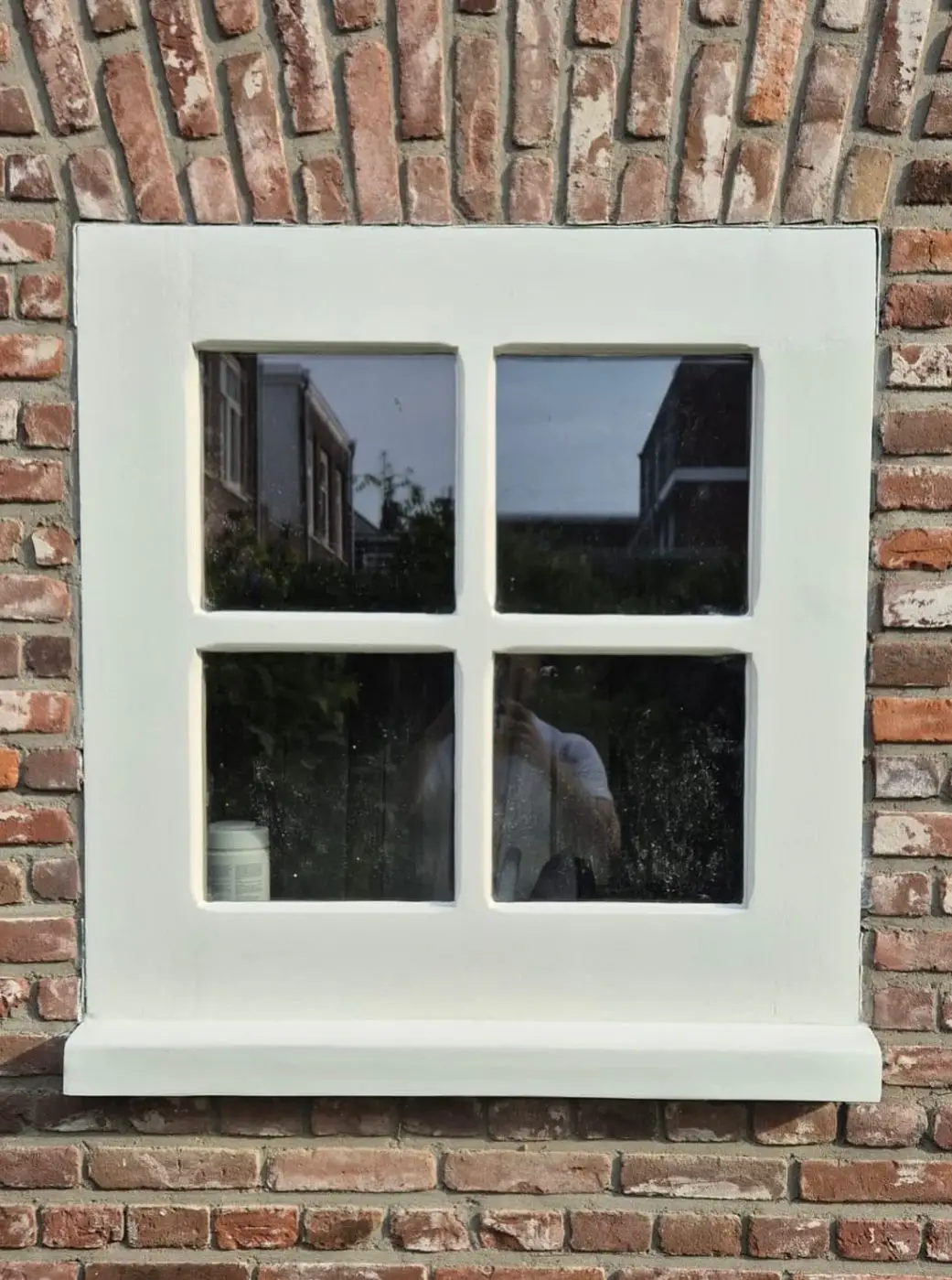 Wit geschilderd houten kozijn met vier ruiten in een rode bakstenen gevel