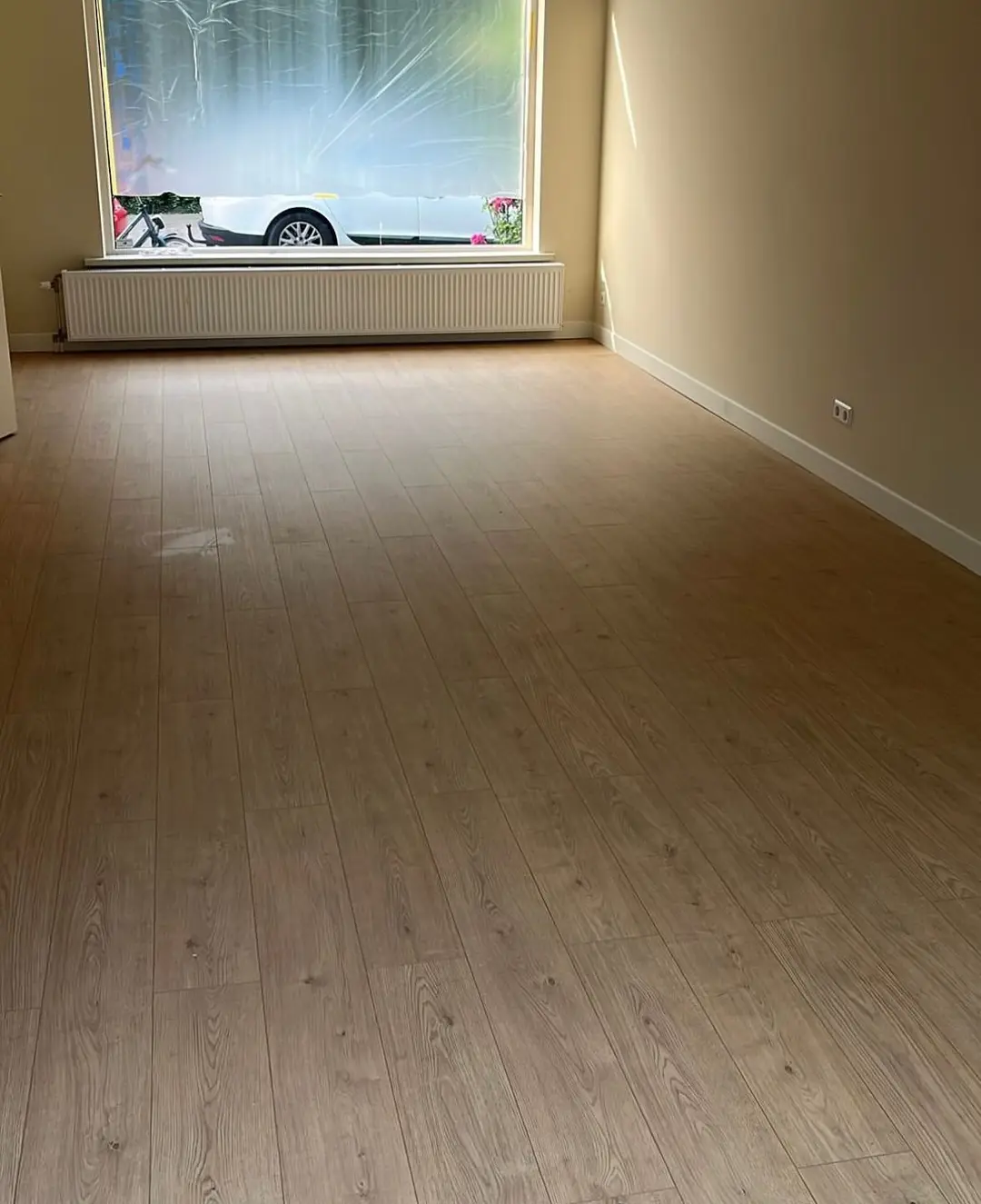 Lege woonkamer met een nieuwe lichte vloer in houtlook, witte plinten en een groot raam