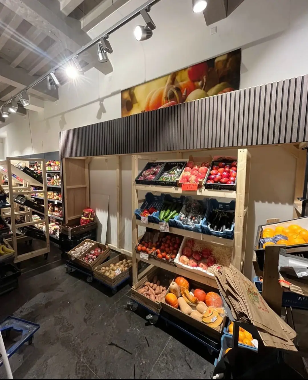 Winkel met houten stellingen vol groente en fruit en een donkere lamellenwand erboven