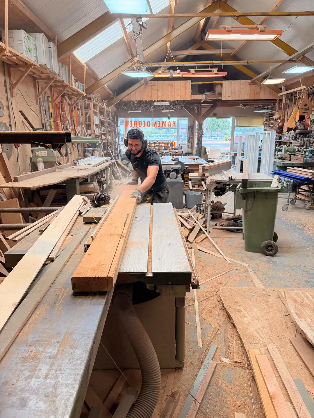 De eigenaar van The Build Company zaagt een houten balk op maat aan de formaatzaag in de werkplaats